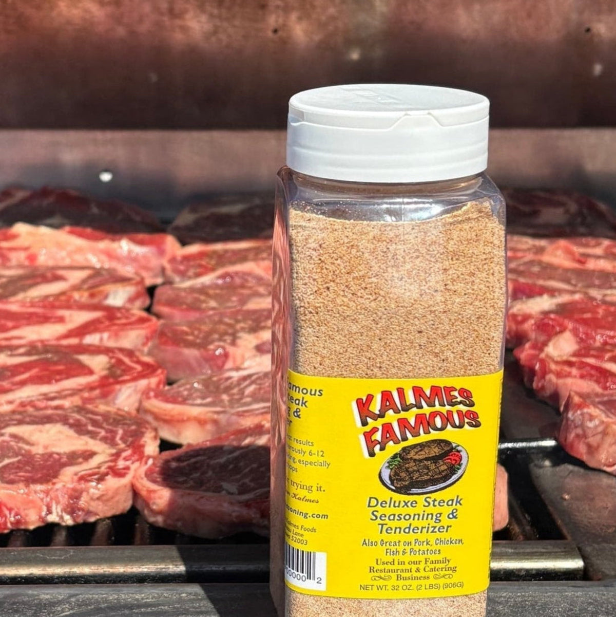 Kalmes Famous® 2-in-1 Seasoning & Meat Tenderizer, 32 oz on a grill ledge with 48 10 oz ribeyes cooking on gas grill