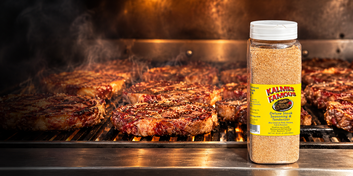 Bottle of Kalmes Famous 2-in-1 Steak Seasoning & Meat Tenderizer in front of steaks cooking on a smoky grill.